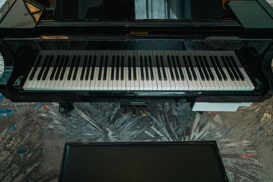Top-down view of a classic black grand piano keyboard showing the black and white keys above the foot pedals and a leather bench.