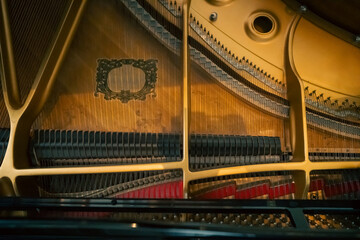 Top-down view inside an acoustic grand piano showing the golden cast-iron plate, tensioned steel strings, and a row of black dampers. © AncientAftertone