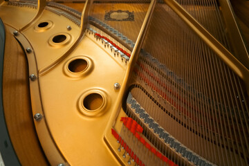 Close-up macro shot inside a grand piano showing the golden cast-iron plate with large circular holes beside tensioned steel strings. © AncientAftertone