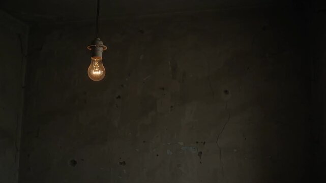Single weak light bulb in dark room representing energy poverty and electricity inequality