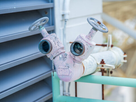 Fire department connection standpipe with twin valves installed on the plumbing line near the building's ventilation louver.