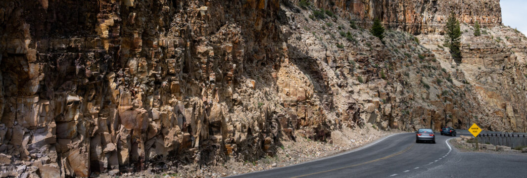 Cars driving on the Grand Loop Road to Kingman Pass by a fractured rock cliff wall, The Golden Gate area, traveling in Yellowstone National Park for summer vacation
