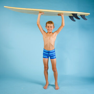 Boy wearing striped swim trunks holding a surfboard over his head