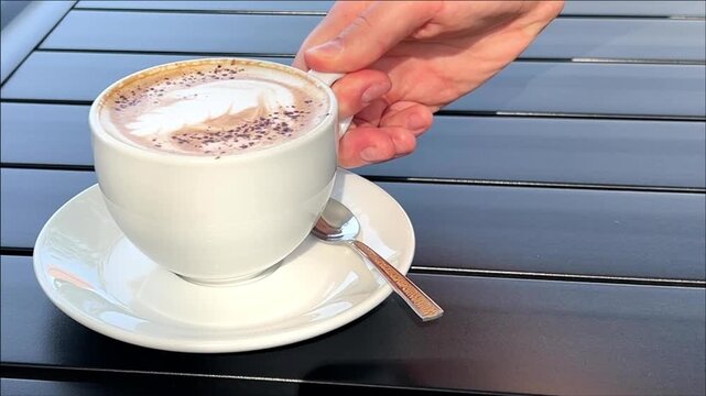 Adult woman holding a white coffee cup above a saucer at an outdoor cafe, relaxed break, coffee culture, casual lifestyle, peaceful leisure.