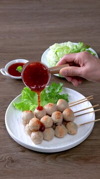 Thai grilled meatballs with sweet and spicy dipping sauce, served on a white plate (Thai street food).	