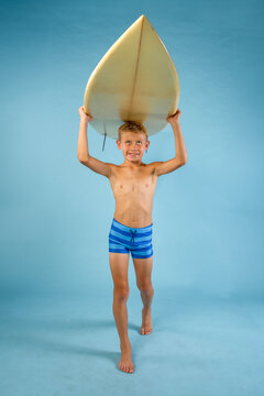 Boy in striped swim trunks carrying a surfboard over his head while walking