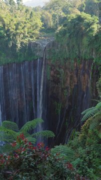 Tumpak sewu waterfall flowing in a tropical rainforest with semeru volcano