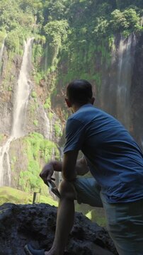 Adventurous man contemplating a beautiful waterfall in nature