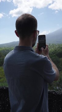 Male tourist taking photos of a volcano with a smartphone