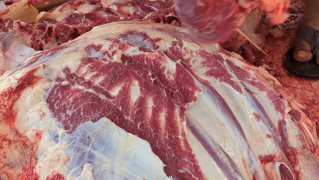 Close-up of a butcher cutting fresh raw beef meat with a sharp knife in a traditional market. High quality red meat with marbled fat.