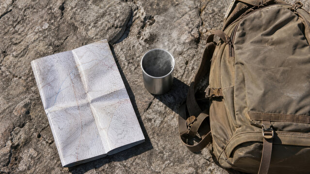 Hiking backpack with map and metal cup on rock