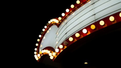 Naklejka premium Curved vintage theater marquee sign with glowing light bulbs against night sky