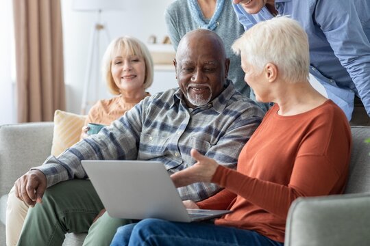 Smiling Elderly African American Man And Woman Sitting Together On Couch, Using Laptop For Communication Or Entertainment At Home, Engaging In Activity With Family. Family Concept.