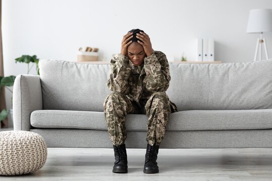 Worried Black Female Soldier Sitting On Couch At Home, Holding Her Head In Hands, Showing Signs Of Distress And Anxiety, Reflecting On Challenges She Faces. Mental Health Concept.
