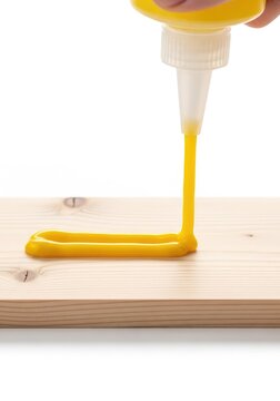 A stream of thick yellow adhesive is carefully applied from a plastic nozzle onto the surface of a light-colored natural timber board, bond, diy, glue