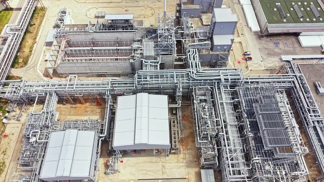 Aerial view of a large industrial site showing multiple buildings and extensive pipe systems. This location is active with various industrial activities occurring during daylight.