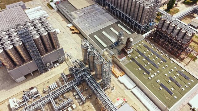 A large industrial site shows multiple storage tanks and machinery. The area has buildings with roofs in various colors. The image captures the structure layout in broad daylight.