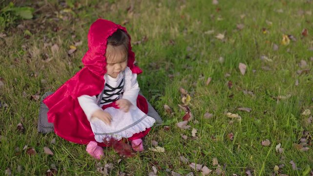 Toddler in Red Riding Hood Costume Playing With Fallen Leaves