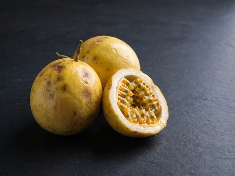 Fresh yellow passion fruit whole and halved showing orange pulp with black seeds on dark stone background
