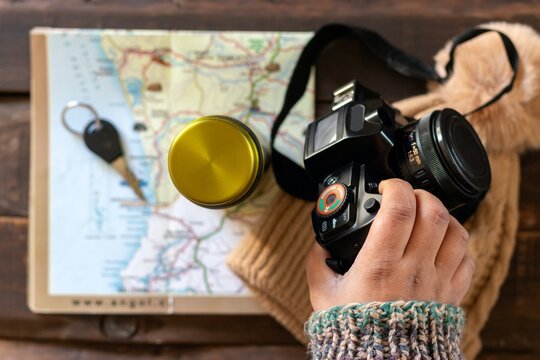 Top view of a travel map with a camera, lens, yellow cup, outdoor gear and warm knit clothing arranged on a rustic wooden table