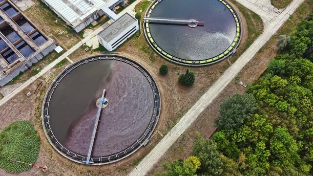 Two large circular tanks sit in an urban area as part of a water treatment facility. Water is being cleaned in full view under clear skies.