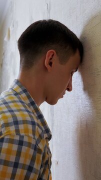 Sad and depressed young man rhythmically banging his head against a wall in despair, symbolizing psychological problems, emotional breakdown, frustration, and a deep life crisis