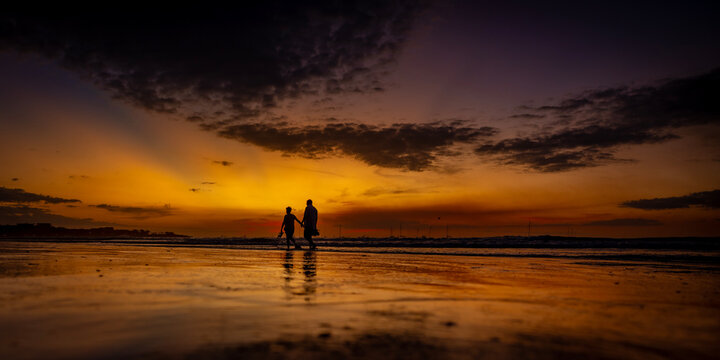 Silhouette of father and son walking hand in hand on a beach at dramatic sunset