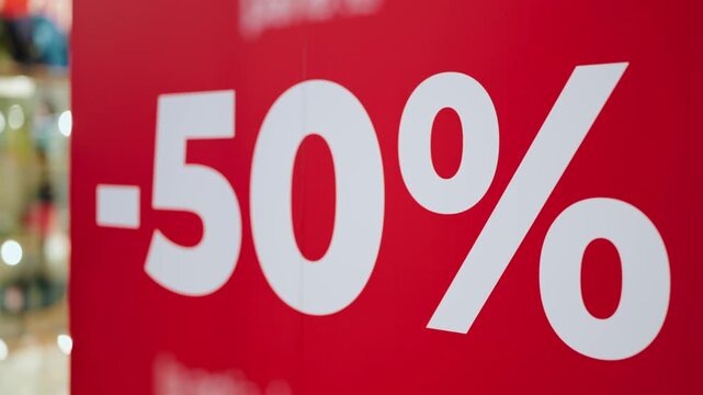 Red banner with fifty percent discount hanging in a shop window during a seasonal sale. This half-price promotion attracts customers looking for a bargain and special offers in the retail store