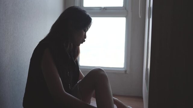 Silhouette of a sad woman sitting alone on the floor by a window