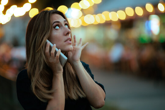 Stressed Woman Covering Ear During Phone Call At Celebration Party. Frustrated lady plugs her ear to hear a smartphone conversation at a noisy evening event