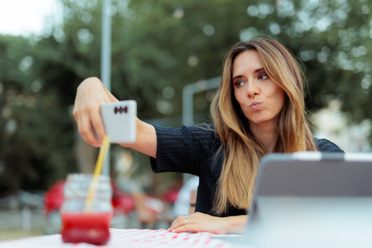  Woman Making Funny Pout Face Expression Taking Selfie Outside. Beautiful lady holds her mobile phone to capture a playful outdoor picture