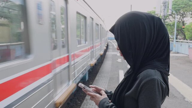 Muslim woman in hijab using a smartphone on a train station platform
