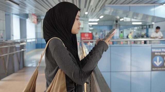 Muslim woman using smartphone at subway station