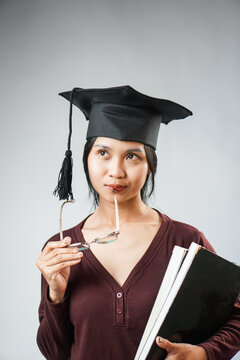 Smiling graduate holding books and graduation cap