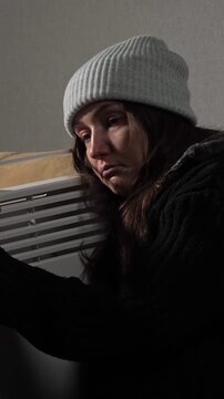 Freezing woman with sad expression trying to keep warm by hugging central heating radiator during winter season, struggling with high utility bills, energy poverty, and gas crisis at home