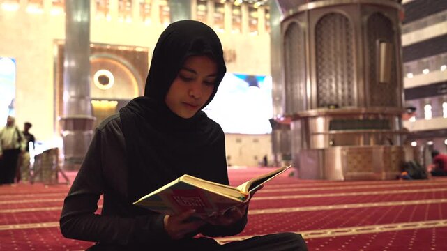 Muslim woman in hijab reading the quran in a mosque