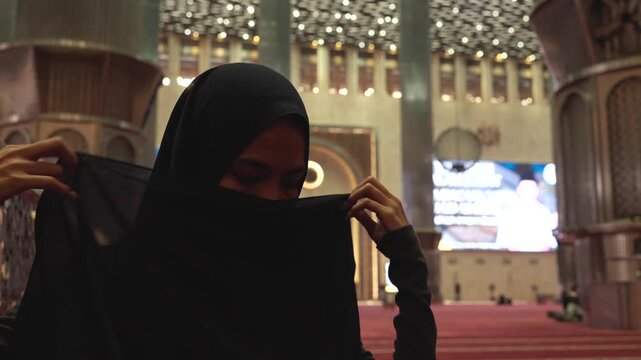 Muslim woman putting on a niqab veil inside a mosque