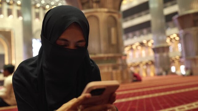 Muslim woman wearing niqab using smartphone inside mosque
