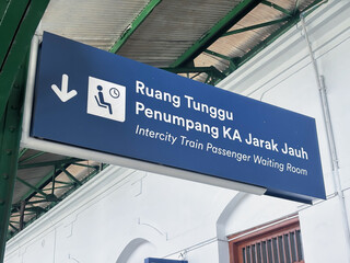 Blue metal signage directional arrow indicates waiting room in indonesian and english languages at a station. Suitable for transportation themed designs. © AriaSandi