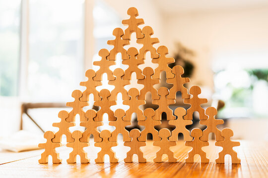 Business hierarchy and teamwork concept with large pyramid stack of wooden people figures on table for corporate organizational structure, team foundation, leadership and scalability.