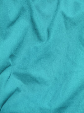 Professional high-resolution photograph of cyan teal woven cotton cloth fabric featuring natural creased folds and detailed thread texture. Ideal target for fashion apparel blogs, textile manfacture