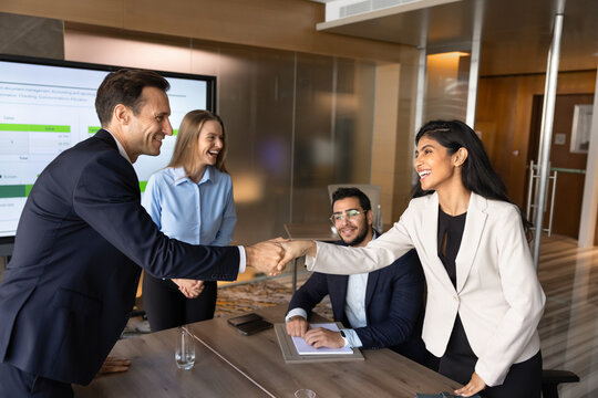 Multiethnic group of businesspeople shaking hands, starting formal meeting, negotiation event in modern conference room. Business deal, partnership agreement and professional collaboration in office