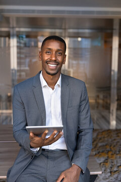Portrait of adult smiling Black businessman holding digital tablet in office, representing business application or platform use, workflow on online project in workplace. Career, skills and technology