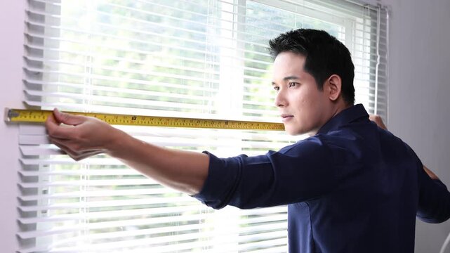 Young asian contractor measuring window width with a measuring tape for blind installation.