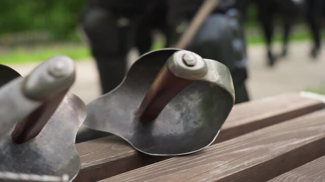 Close up of metal practice swords with red felt padding resting on wooden bench. hand briefly adjusts one sword revealing detailed craftsmanship including engraved initials and textured