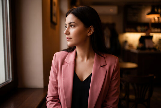 Young Asian woman in pink blazer looking out window thoughtfully