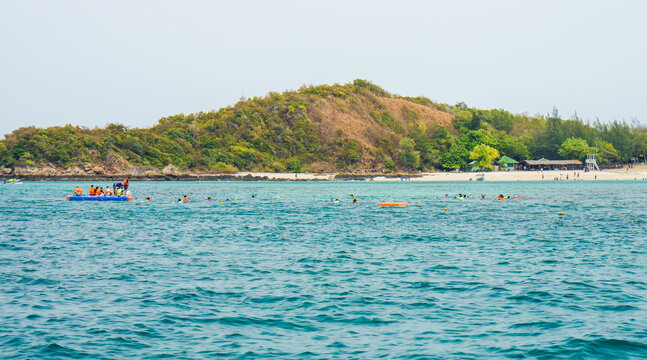 Tourists snorkeling in sea near Luk Lom Beach at Ko Samae San Island. View of tourists wearing orange life jackets snorkeling near floating raft off Luk Lom Beach in Sattahip, Chon Buri, Thailand.