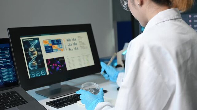 Female scientist examines a petri dish and analyzes DNA sequencing data on a monitor