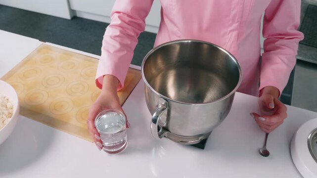Close-up video of pouring water into a stand mixer during the preparation of ingredients for homemade French macarons. Baking and pastry making process in a kitchen.
