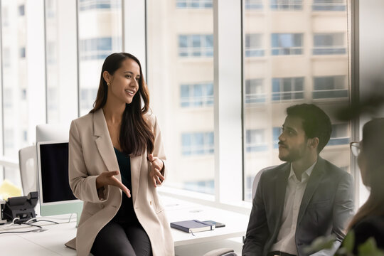 Female team leader explaining strategy, express ideas, share solutions to diverse colleagues during office discussion. Business communication, professional collaboration on project, corporate briefing